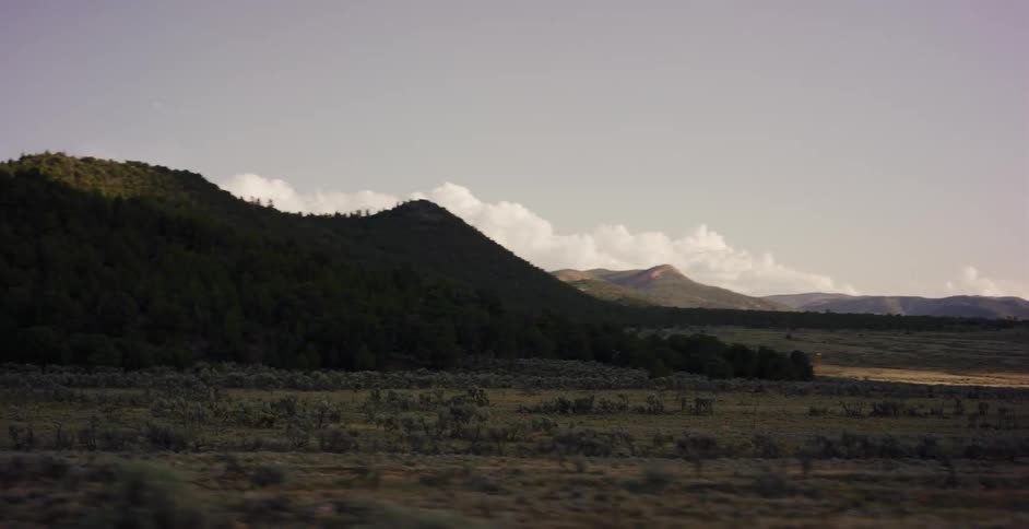 A slow tracking shot reveals a vast and serene landscape of rolling, tree-covered hills and plains at dusk