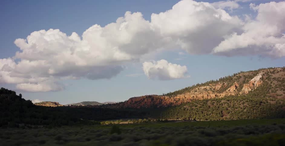 A beautiful rolling landscape of green fields and sunlit hills passes by during a scenic drive