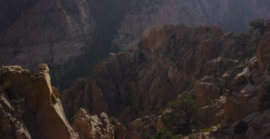 A slow zoom out reveals the immense and rugged landscape of a sunlit mountain canyon