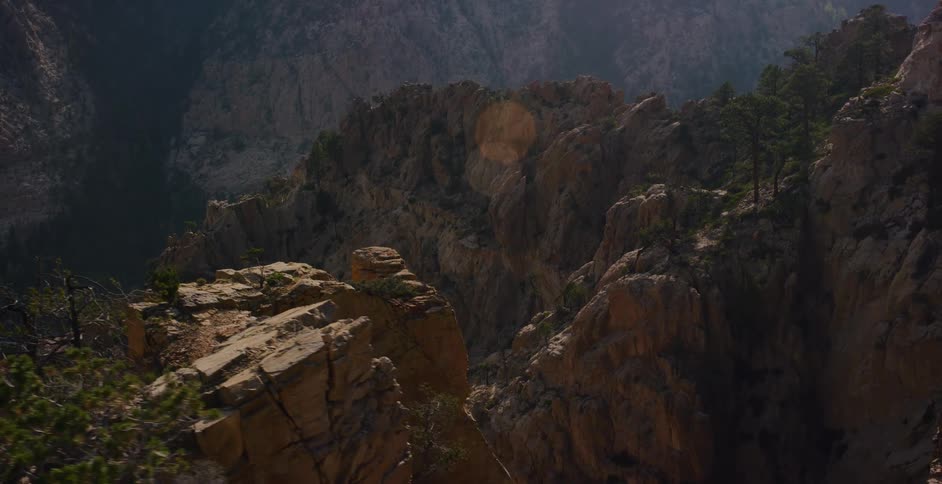 A slow revealing shot of a sun-drenched, rugged mountain canyon, with pine trees dotting the rocky landscape
