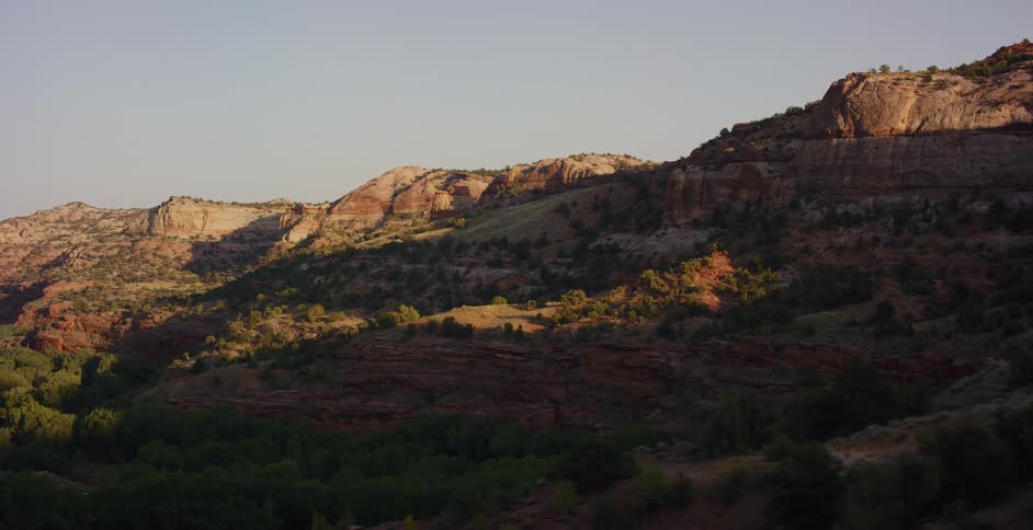 A subtle time-lapse shows golden sunrise light moving across a rugged desert canyon