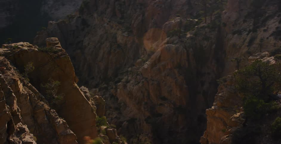 A slow zoom out from a rocky mountainside reveals a vast and majestic sun-drenched canyon
