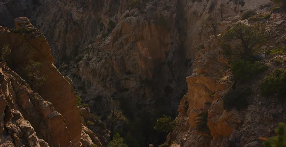 A slow pan reveals the majestic and rugged terrain of a rocky canyon illuminated by the golden light of a hazy sunrise