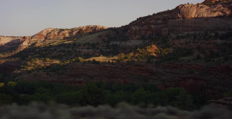 A tracking shot across a vast desert canyon as the morning sun illuminates the red rock formations