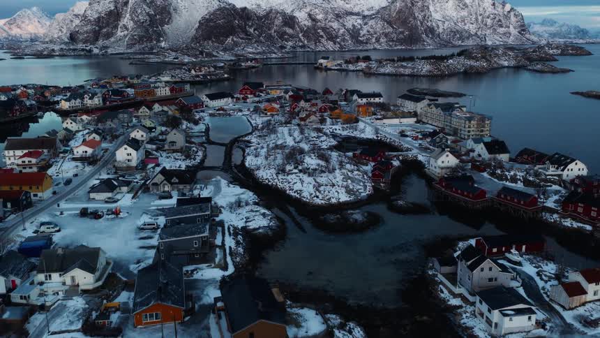 A stunning aerial flight over a snow-covered fishing village in Norway reveals a dramatic, majestic mountain range across the water