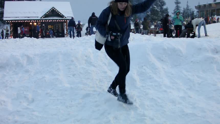 A woman carrying a camera tries to walk down a snowbank