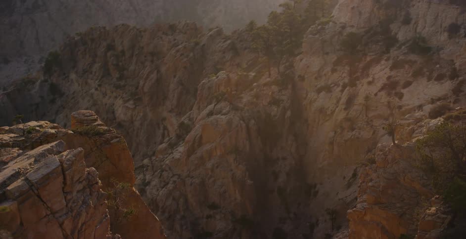A slow cinematic pan reveals the vast and rugged beauty of a sun-kissed canyon landscape dotted with pine trees