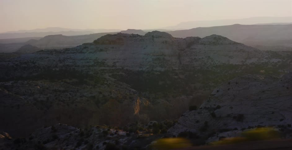 A scenic point-of-view from a moving vehicle captures the vast, hazy desert canyon landscape at sunset