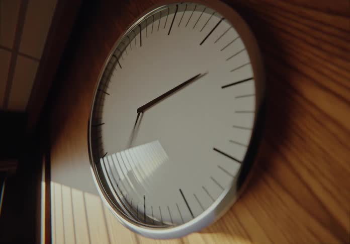 A dramatic timelapse of a simple wall clock on a wood-paneled wall as the hands spin rapidly and the light changes from day to night