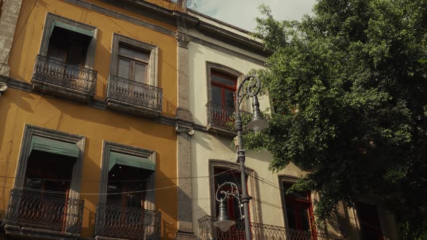 Sunlight casts shadows across the facade of a beautiful, historic colonial-style building in a vibrant city