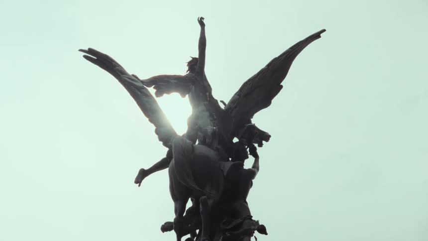 The bright sun flares from behind a dramatic silhouetted statue of a winged angel