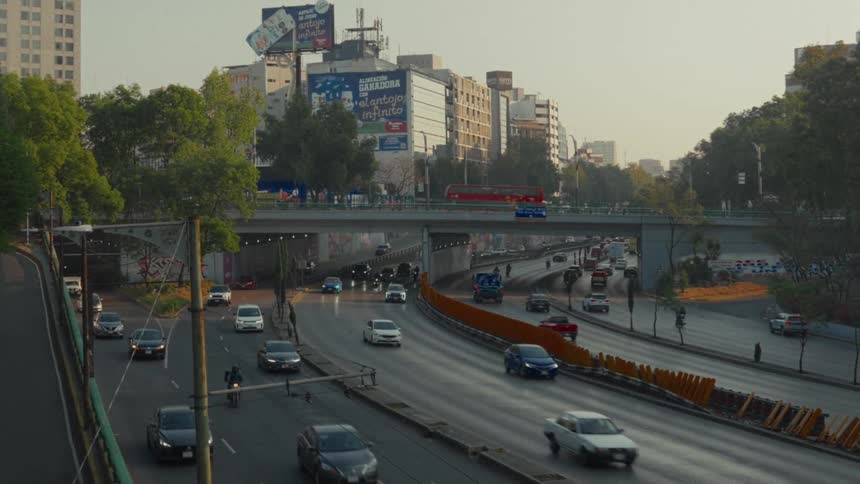 A static high-angle view captures the continuous flow of traffic on a multi-lane highway in a bustling city during the golden hour