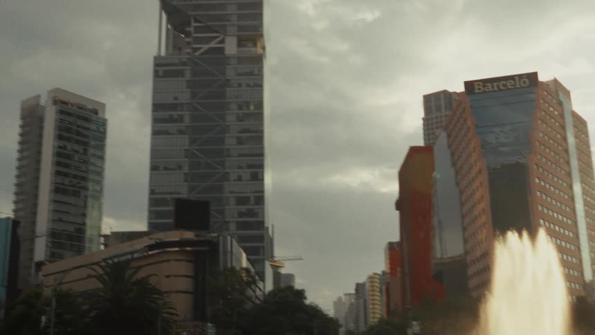 A pan and tilt up from a sunlit city roundabout with a fountain reveals the impressive Torre Reforma skyscraper in Mexico City