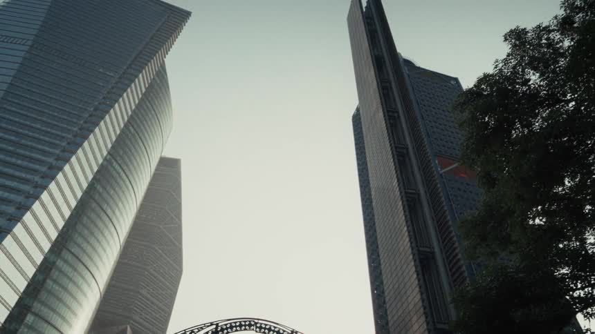 A low-angle shot pans slowly across the imposing glass facades of modern skyscrapers reaching towards the sky