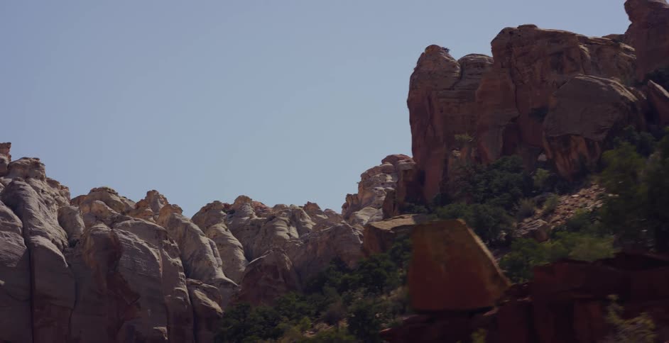 A slow panoramic view of rugged red and white sandstone cliffs in a desert canyon under a clear sky