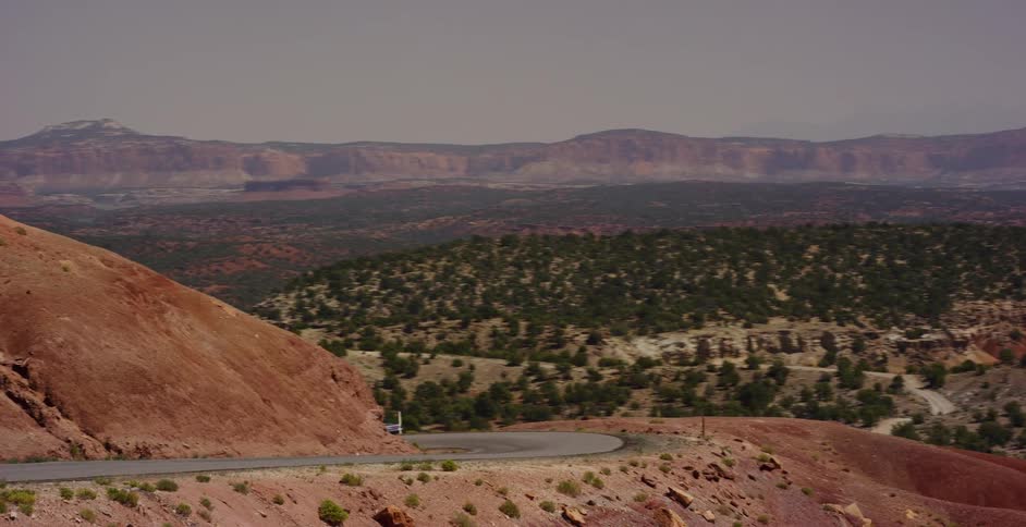 A classic pickup truck drives along a scenic highway winding through a vast and remote red rock desert landscape
