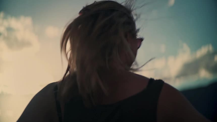 Slow motion shot of a joyful woman with sunglasses turning and smiling as her hair whips through the air in the golden hour light