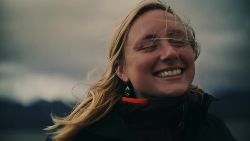 A smiling blonde woman feels the wind blow through her hair in a dramatic slow-motion close-up