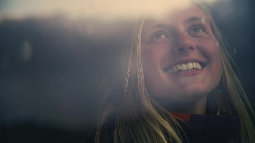 Dreamy slow motion shot of a happy young woman looking out a window as rain or snow falls