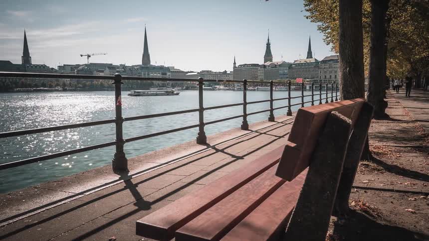 A dynamic timelapse from a park bench shows people passing by along the sunny Alster Lake waterfront in Hamburg, Germany