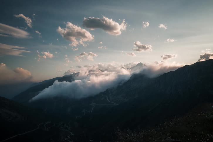 A stunning time-lapse captures clouds cascading like a waterfall over a dramatic mountain range at sunset