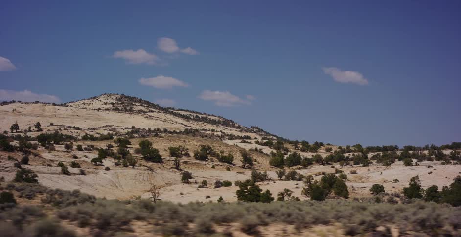 A serene, slow-moving shot captures the vast, arid landscape of a desert with sandy hills and sparse vegetation under a clear blue sky