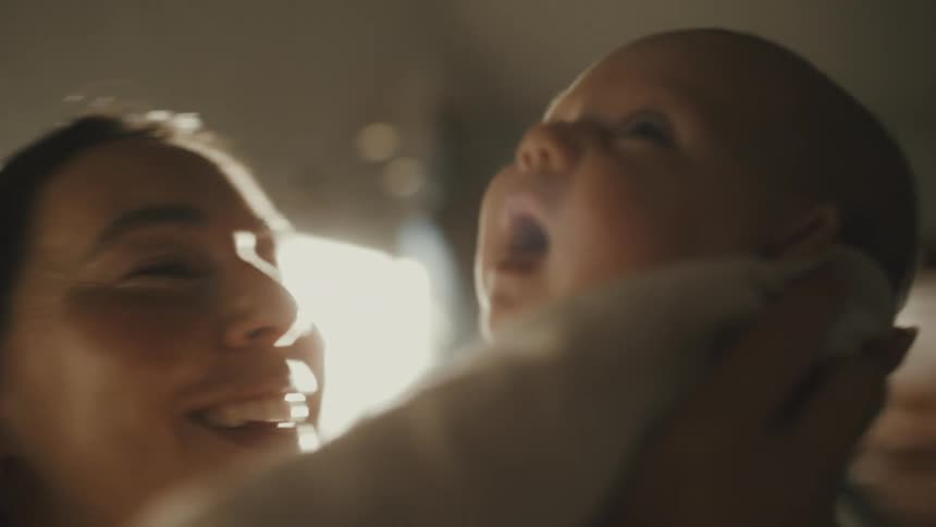 An intimate and heartwarming close-up of a loving mother kissing and holding her yawning newborn baby in a sunlit room
