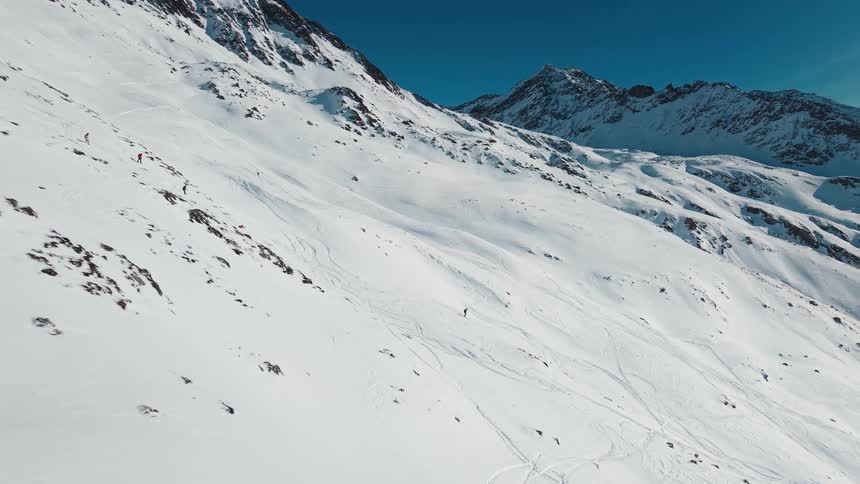 An epic aerial view follows multiple skiers as they carve down a vast, snow-covered mountain on a beautiful sunny day
