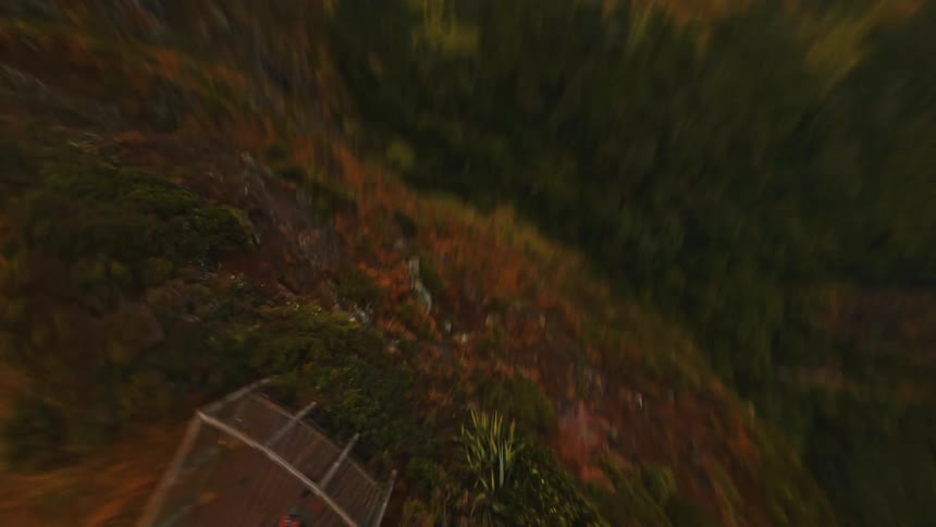 An FPV drone performs a thrilling dive down a rugged coastal cliff, flying over a lone person on a scenic viewpoint