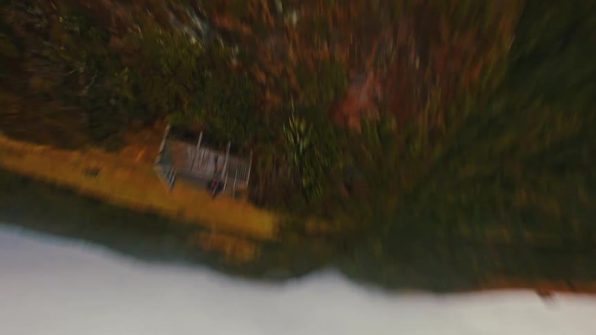 Dynamic FPV drone hyperlapse flies toward a person on a coastal lookout point before performing an acrobatic flip to reveal the dramatic shoreline