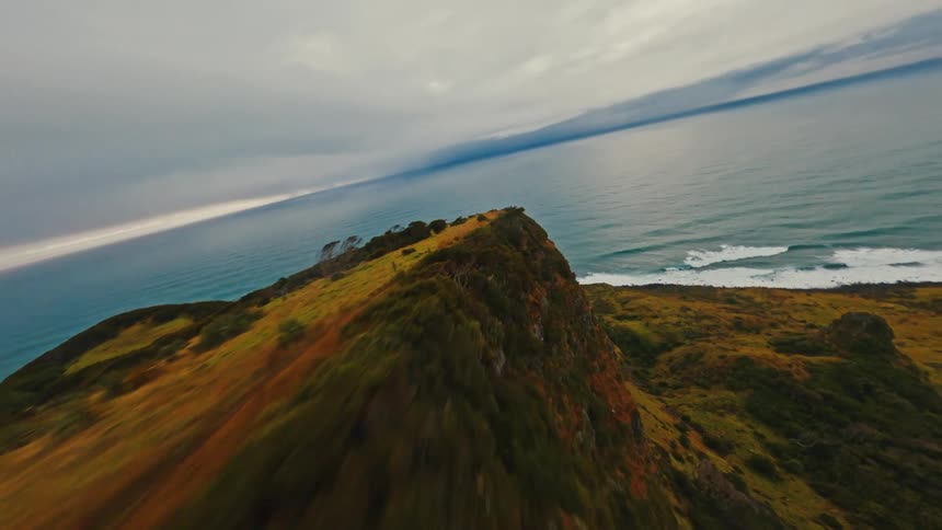 Dynamic FPV drone footage captures a fast flight over a windswept cliff edge next to the sea on an overcast day