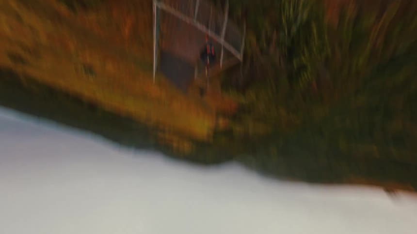 A fast-paced FPV drone shot soars over a grassy cliff, approaches a person on a viewpoint, and then performs a thrilling dive down the mountainside towards the sea