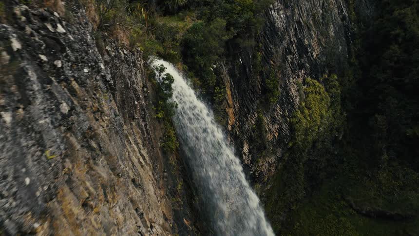 An awe-inspiring aerial view captures a powerful waterfall plunging down a rugged cliff face in a lush, green forest