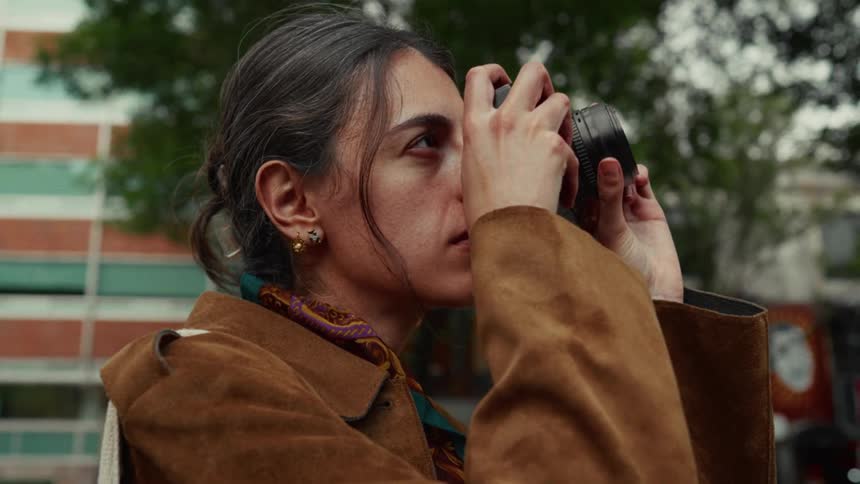 A focused female photographer raises her camera to take a picture on a city street in slow motion