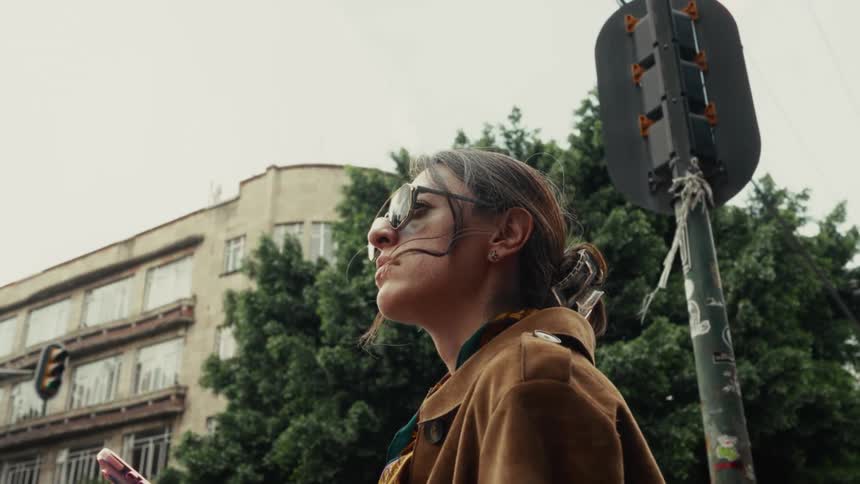 A stylish woman in slow motion checks her phone on a busy city street corner before looking up and away