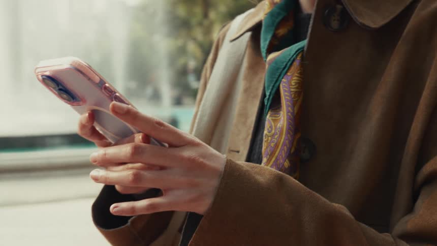 Close-up of a stylish woman's hands scrolling through her smartphone while standing by a city fountain