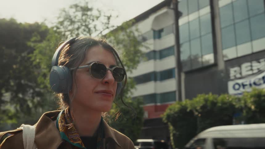 A stylish woman in sunglasses and headphones enjoys listening to music while walking down a sunny city street