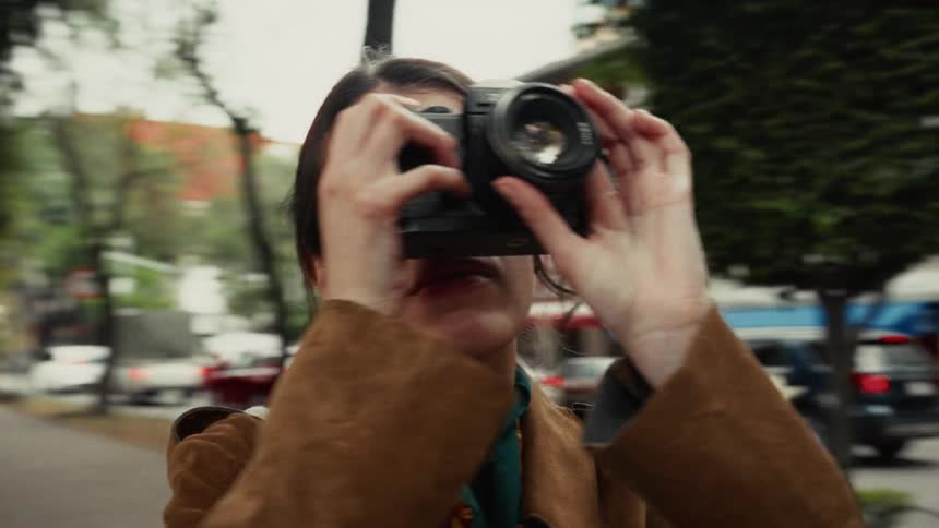 A female photographer with a vintage camera captures a moment on a city street in a dynamic orbital shot