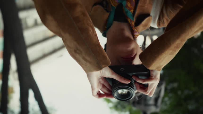 Dynamic rotating slow motion shot of a stylish female photographer taking pictures with her camera in a city square