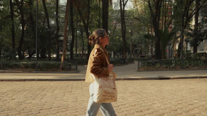 Slow motion of a stylish woman walking through a sunny city park as a dog runs past