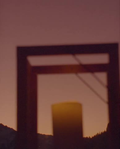 An out-of-focus basketball hoop is silhouetted against a hazy, purple and orange sunset sky