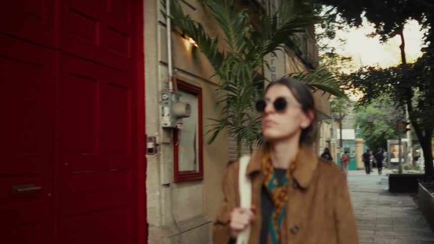 A stylish young woman in sunglasses walks confidently down a city sidewalk in slow motion