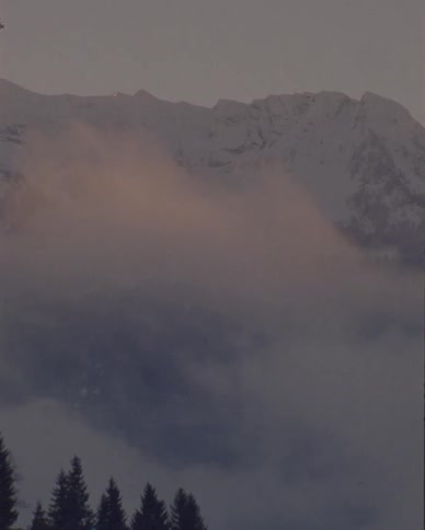 Low-lying fog with a warm glow moves across a snowy mountain landscape at twilight