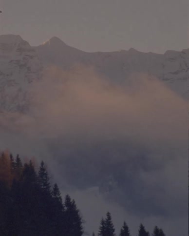 A serene, slow pan reveals a majestic, snow-covered mountain range veiled in mist during golden hour