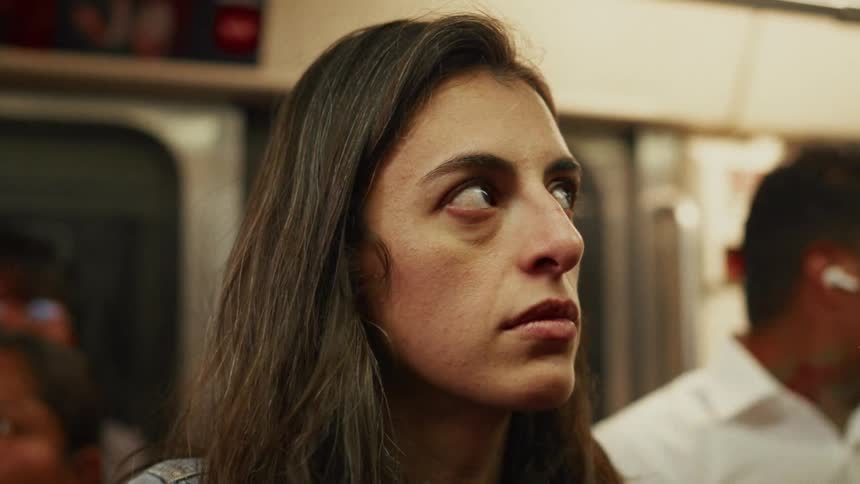 A weary woman with a blank expression commutes on a crowded subway train