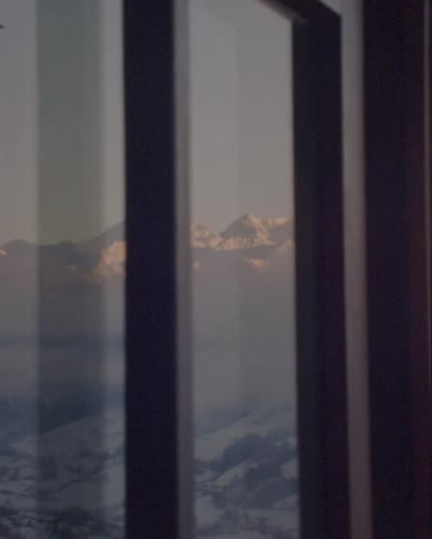 A panning shot reveals a stunning view of a snow-covered mountain range at sunrise from a cabin window