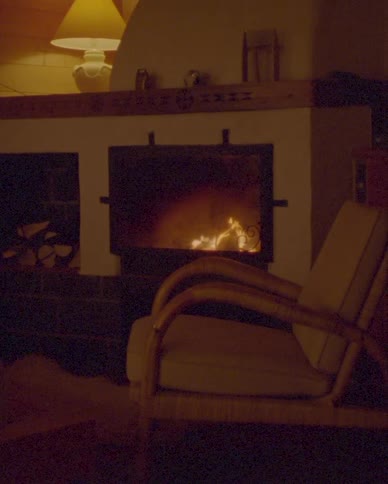 A slow zoom-out reveals a cozy armchair in a rustic cabin, warmed by the gentle flames of a fireplace
