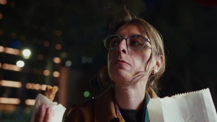 Close up slow motion shot of a thoughtful woman eating a churro on a city street at night