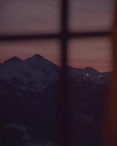 A slow pan from a window reveals a serene snowy mountain range as the last light of day fades