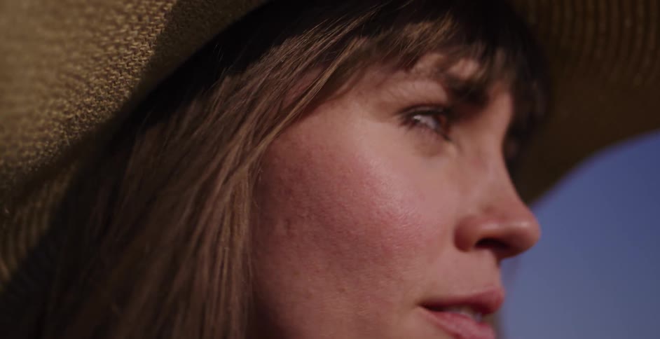Intimate close-up of a beautiful woman in a hat, her face illuminated by warm sunlight as she looks away thoughtfully